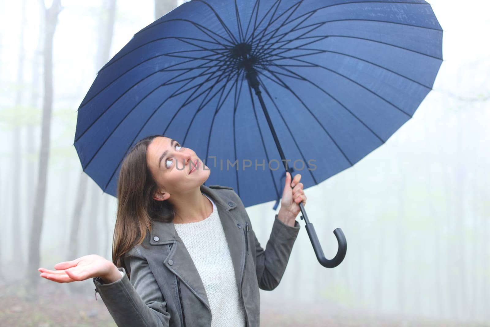 Happy woman under unbrella a rainy day looking above in a foggy forest