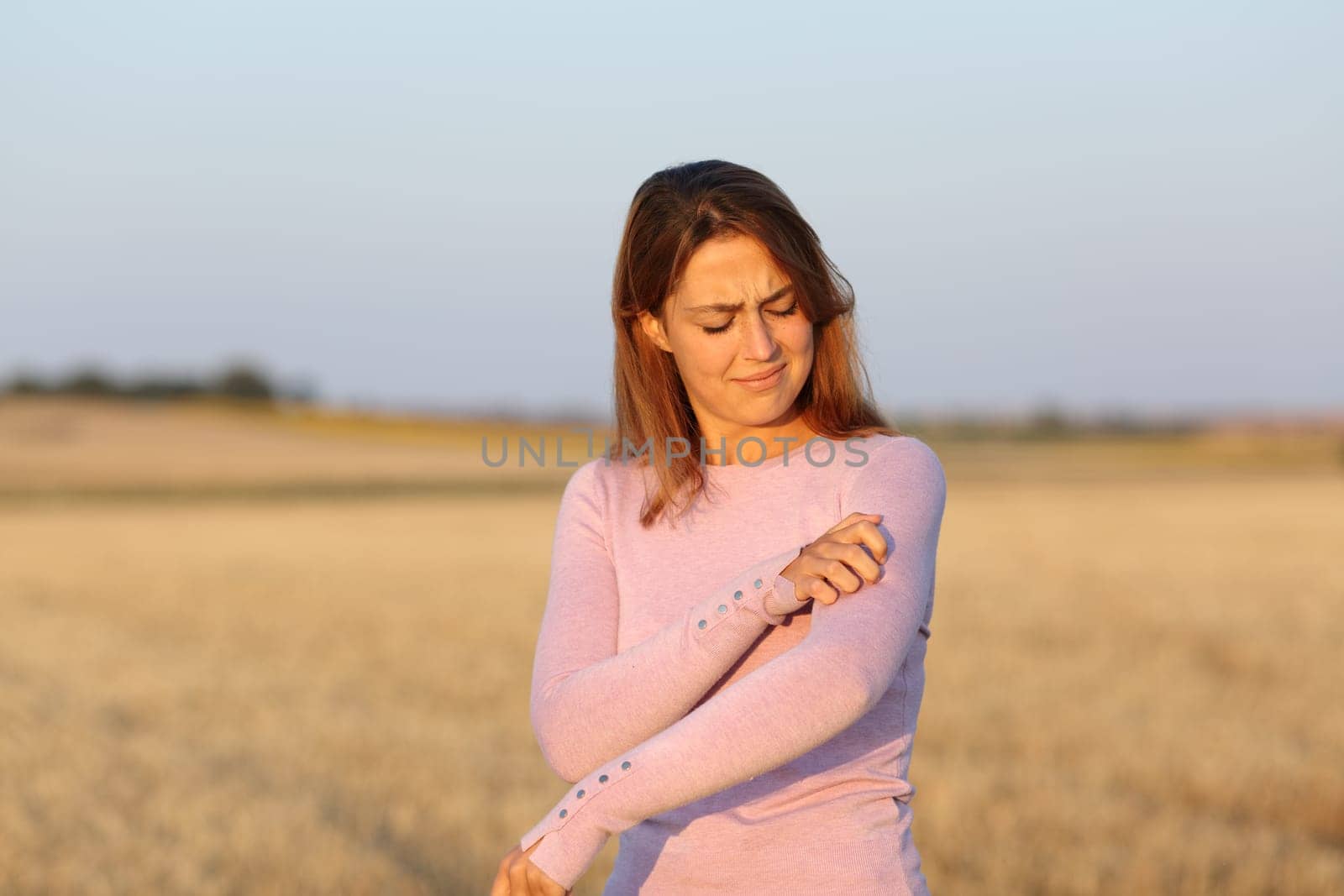 Stressed woman scratching itchy arm in a harvested field