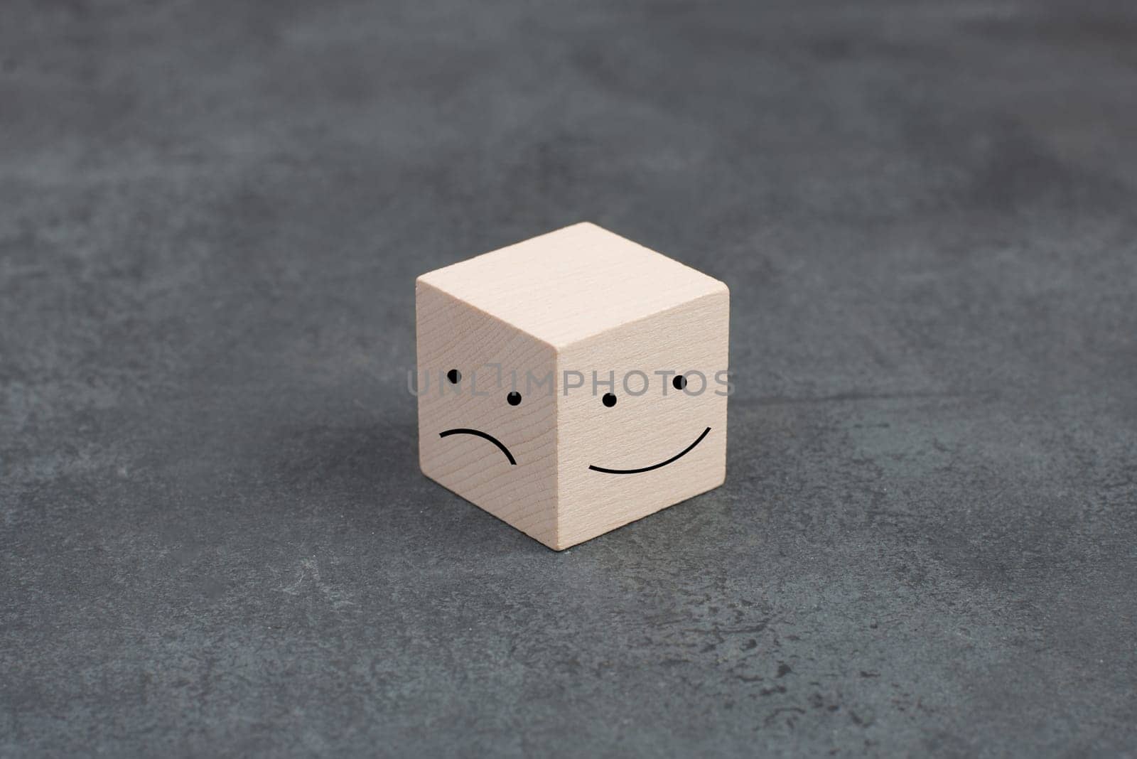 One wooden cube with a smiling and a sad face on a dark background, symbol