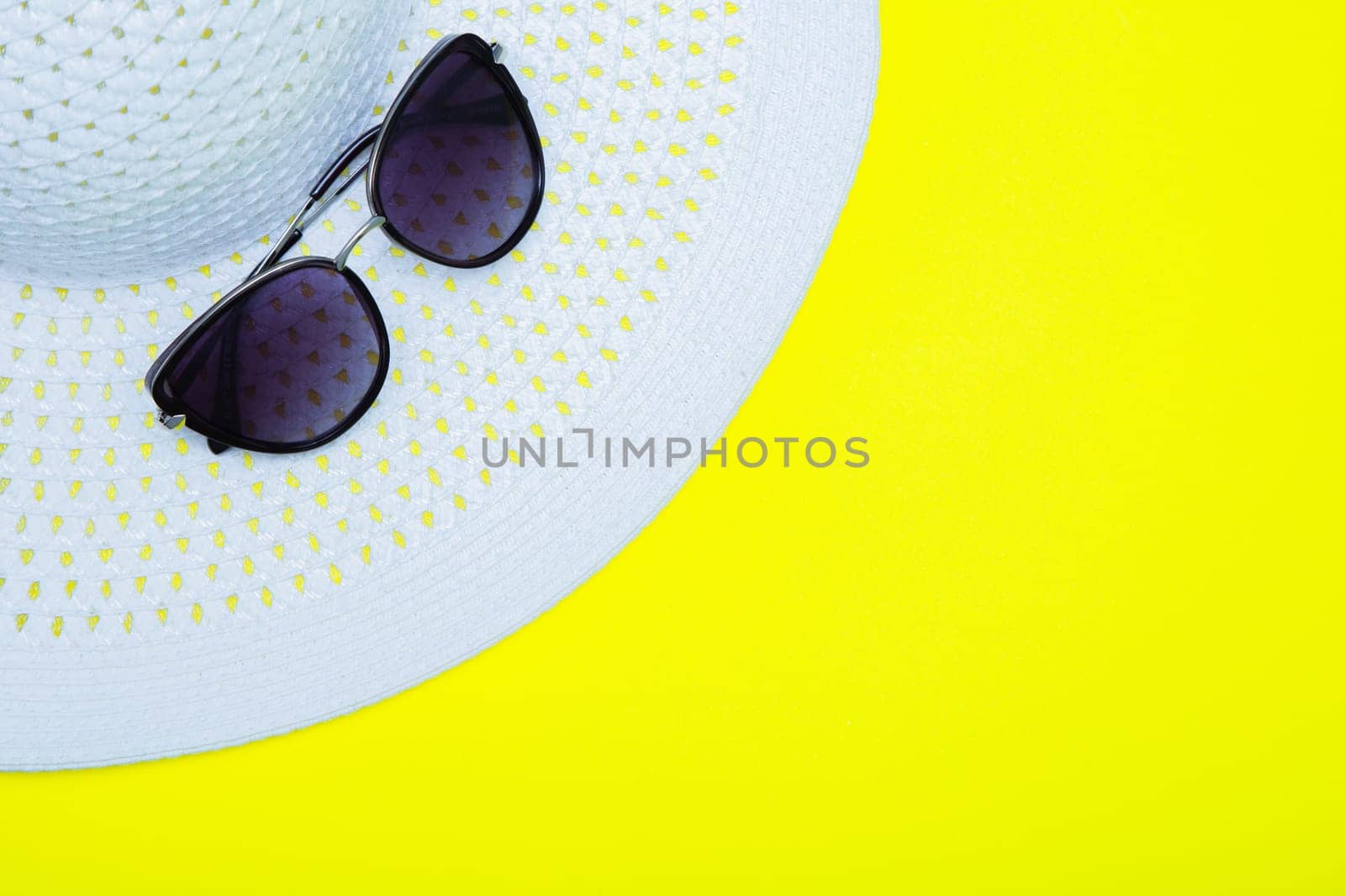 On a white sun hat with a wide brim are sunglasses on a yellow background with a place for text. High quality photo