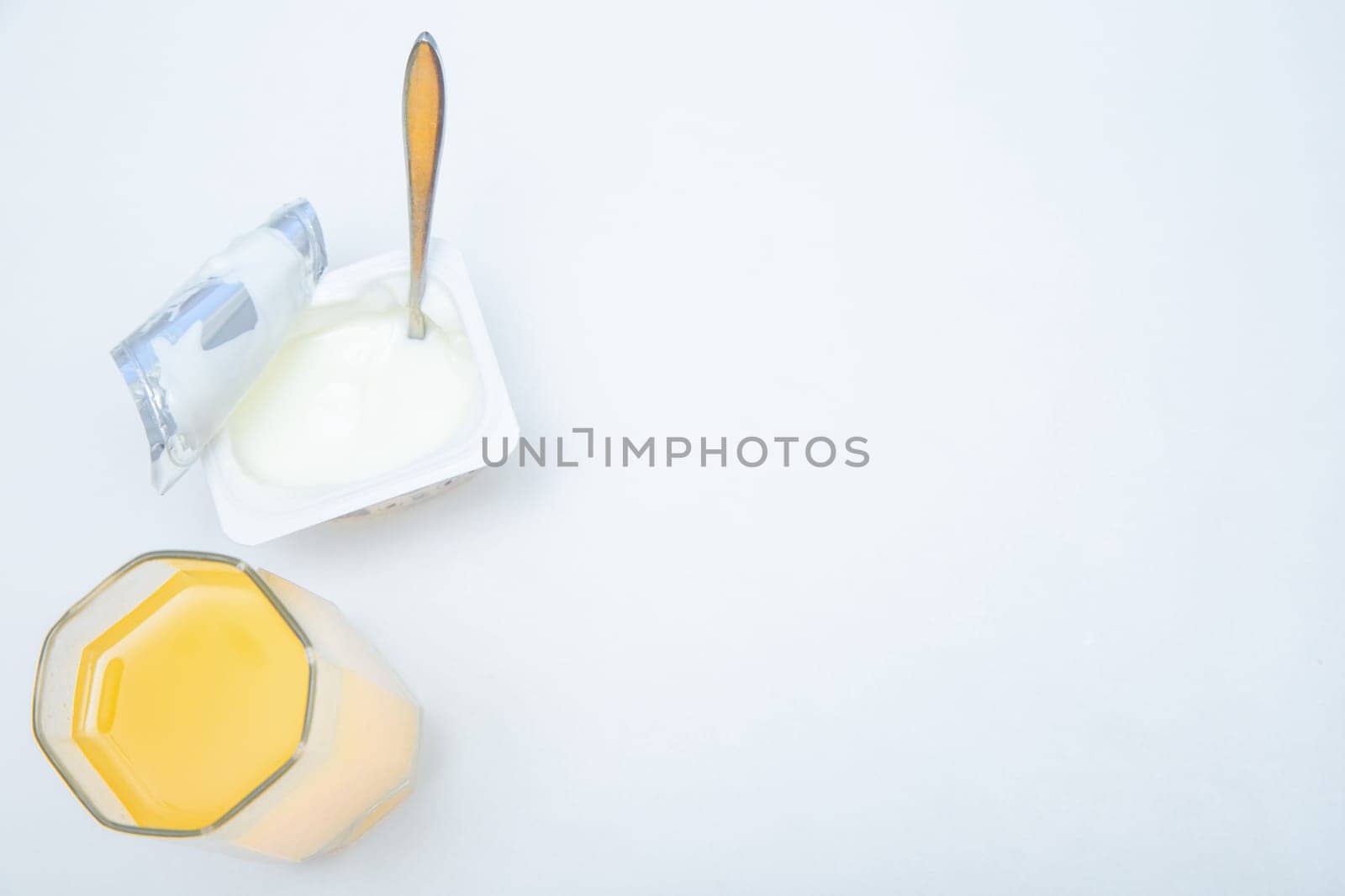 A cup of natural yogurt, a dessert spoon and a glass of orange juice on a white background. High quality photo