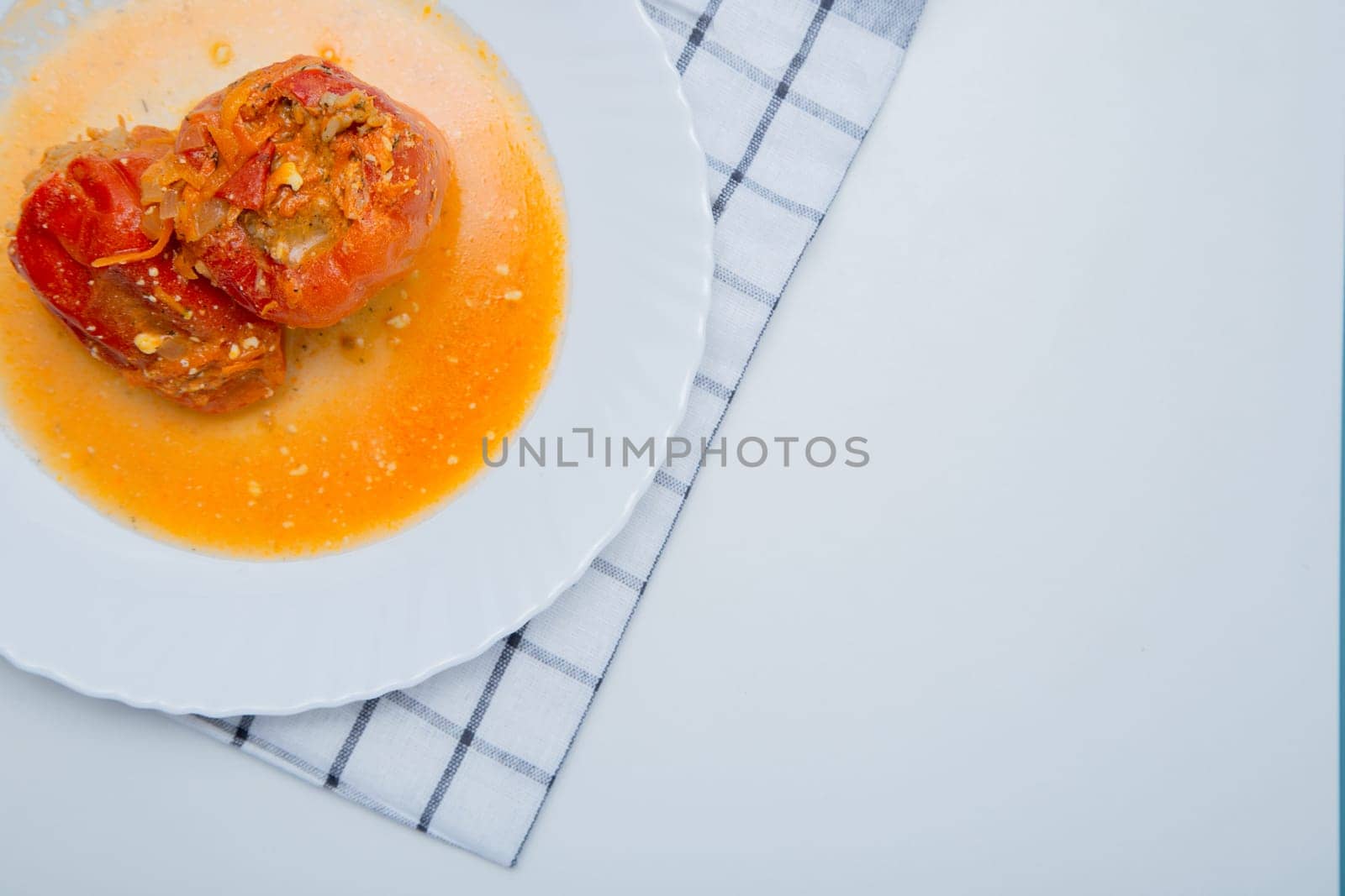 Red pepper stuffed with minced meat and carrots with onions lies on a white plate, which stands on a waffle napkin on a white background. High quality photo
