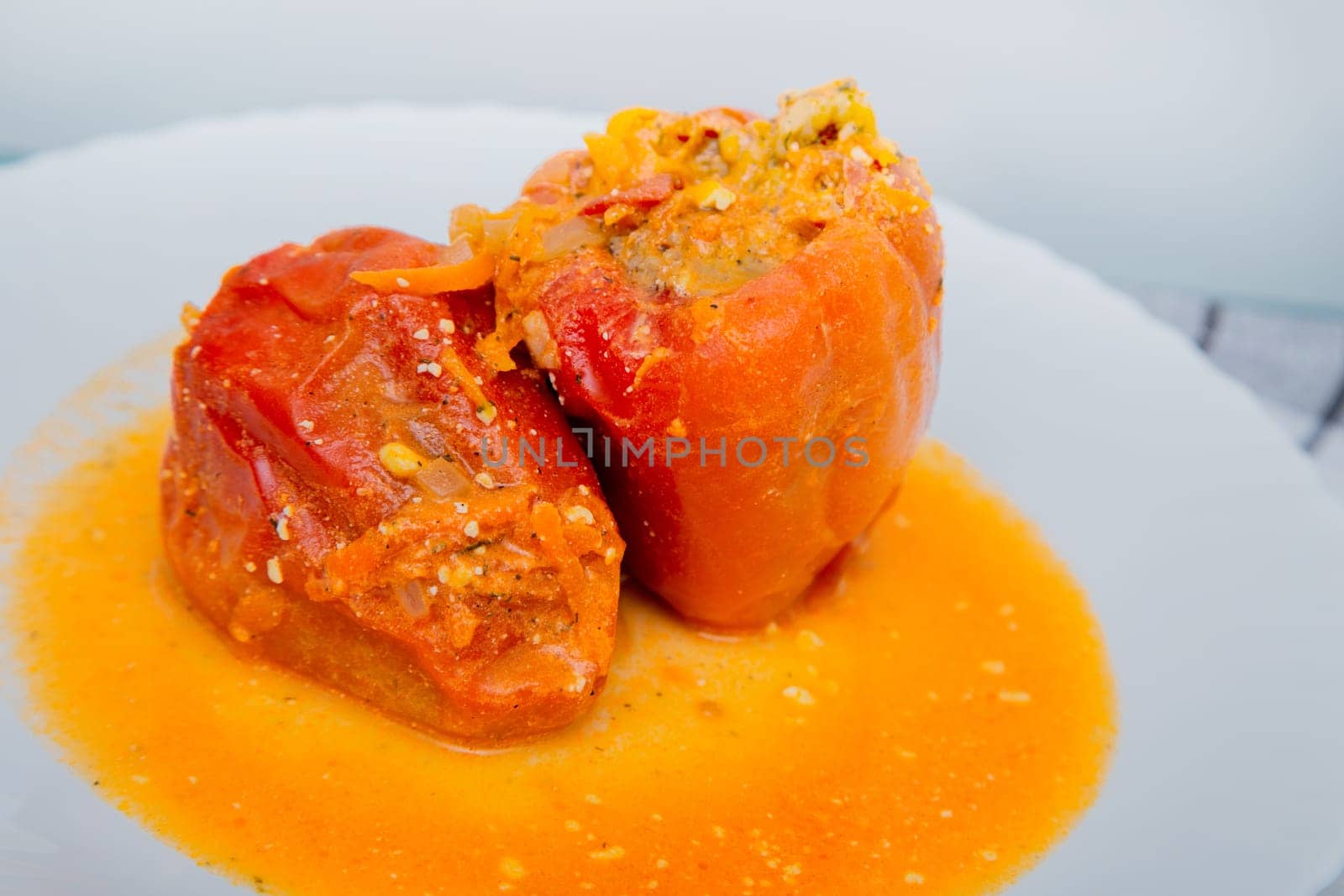 Red pepper stuffed with minced meat and carrots with onions lies on a white plate, which stands on a waffle napkin on a white background. High quality photo