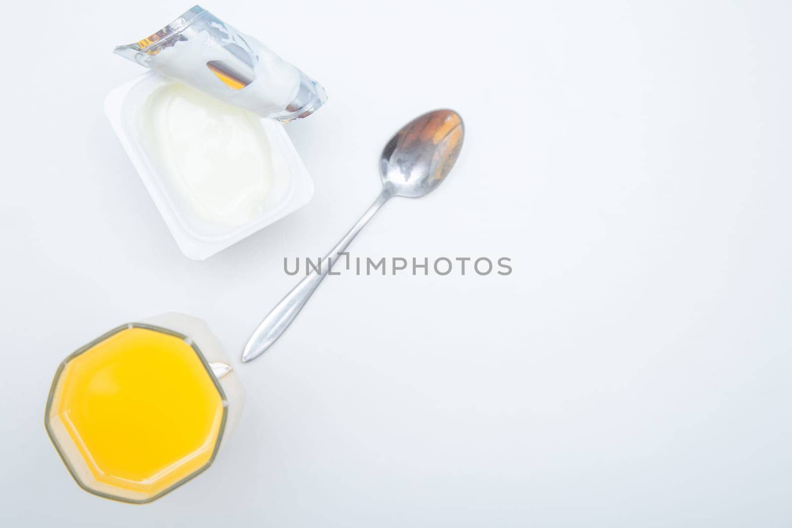 A cup of natural yogurt, a dessert spoon and a glass of orange juice on a white background. High quality photo