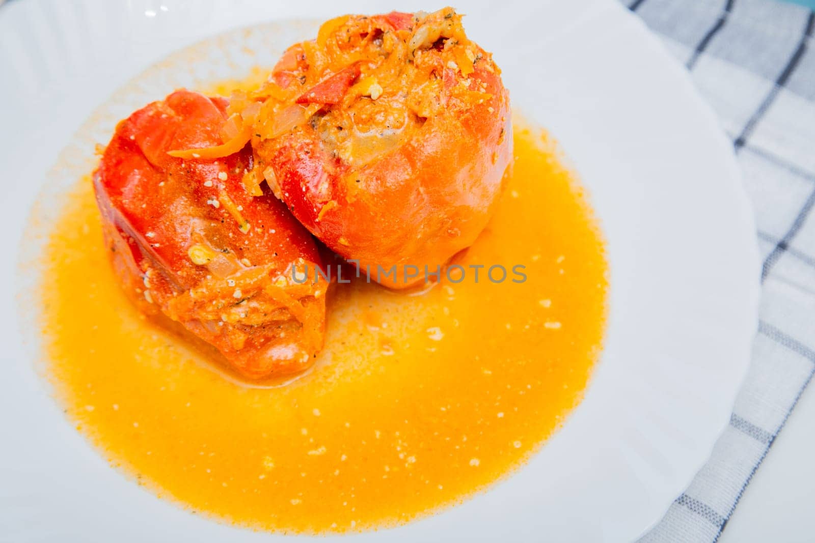 Red pepper stuffed with minced meat and carrots with onions lies on a white plate, which stands on a waffle napkin on a white background. High quality photo