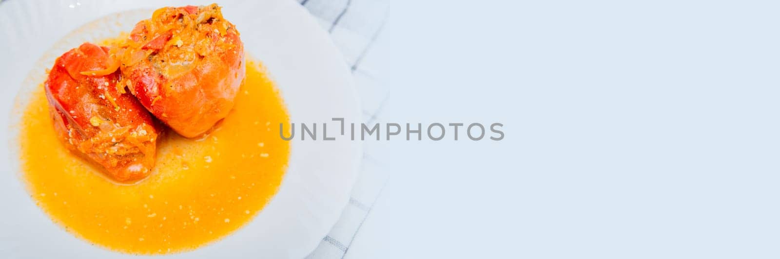 Red pepper stuffed with minced meat and carrots with onions lies on a white plate, which stands on a waffle napkin on a white background. High quality photo