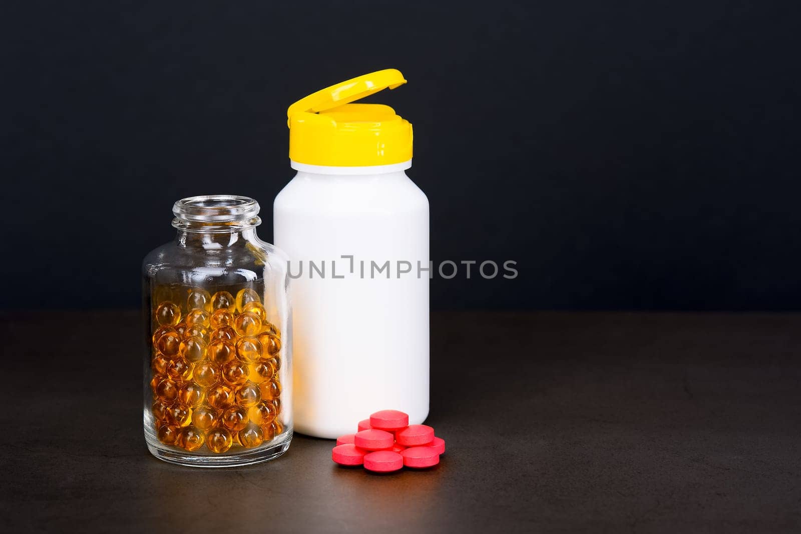 A glass jar with bright yellow tablets and a white pill jar on a brown background. Place for the label, logo, layout.