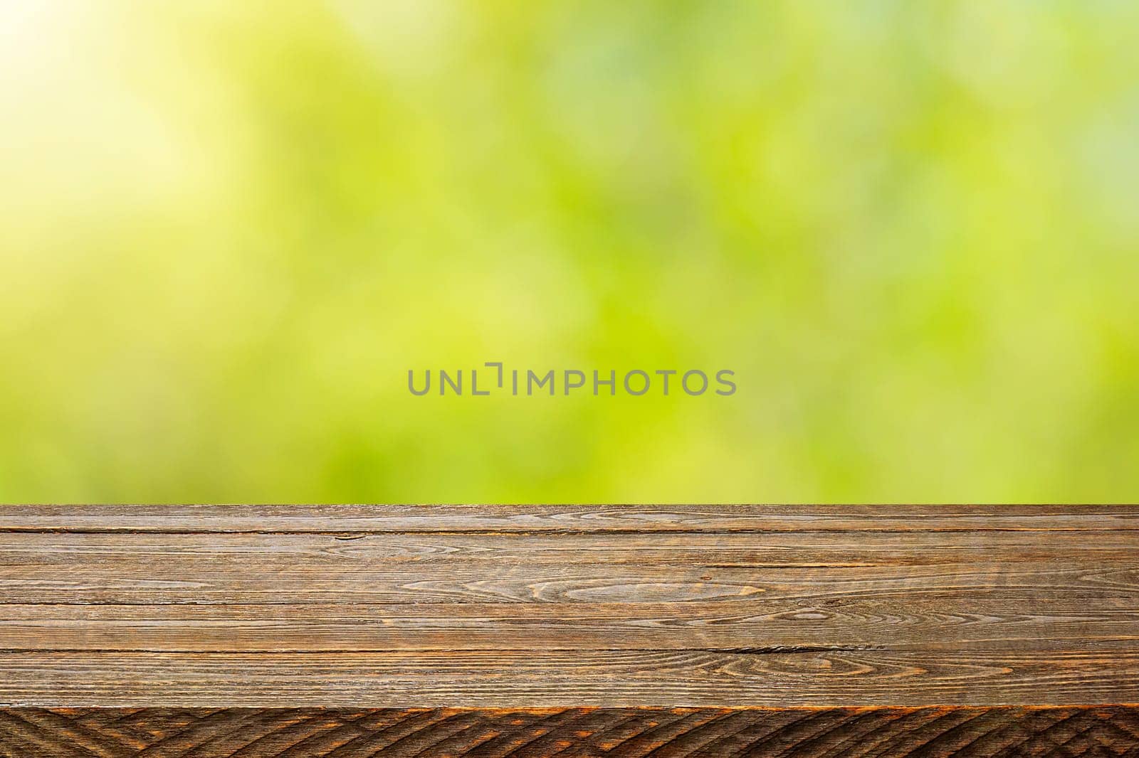 Background with blurred green leaves and empty wooden planks in the foreground. For product demonstrations, free space, layout, mockup, perspective board, background board.