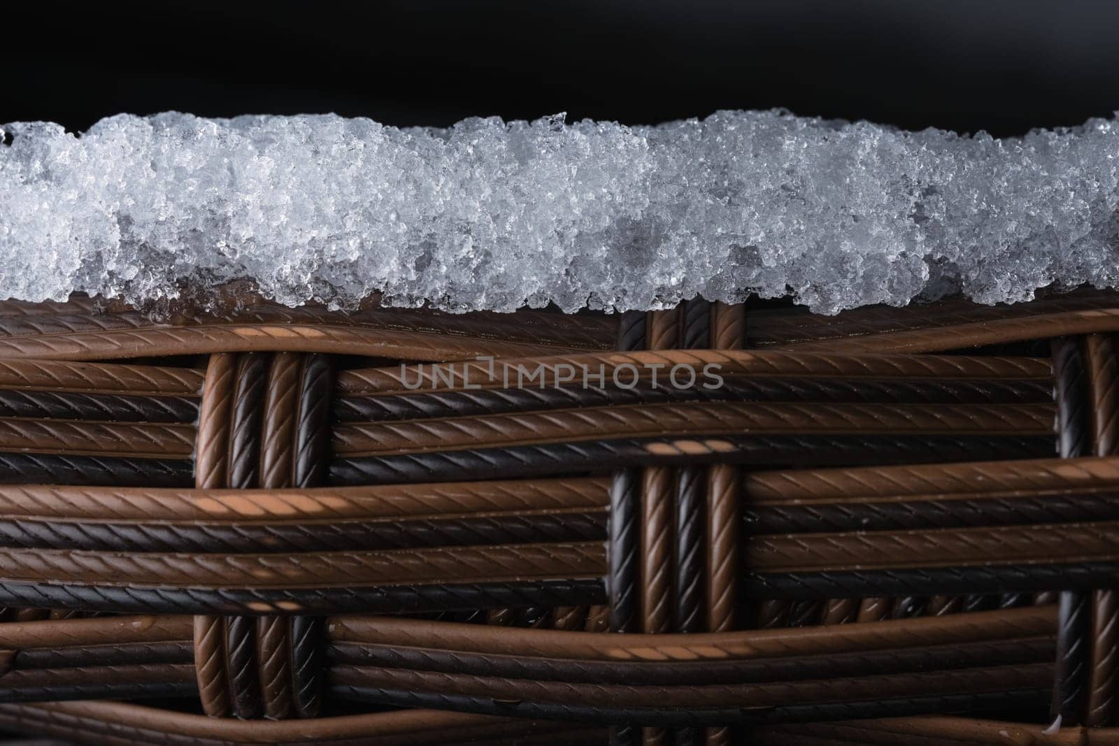 Layer of ice sits on top of textured plastic garden furniture. Copy space over black backgruond, full frame composition. Rope like macro appearance