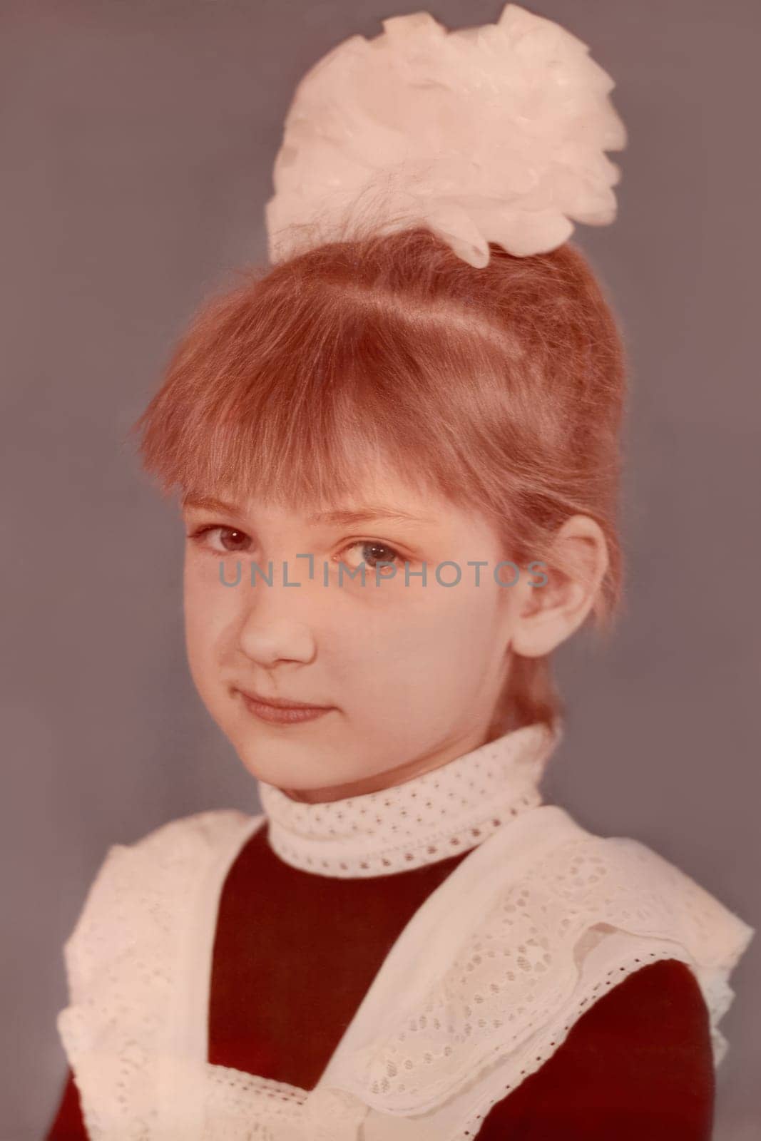 First-grader girl, seven years old, with a bow on her head and in a school uniform, white apron. Vintage photo from 1988. USSR