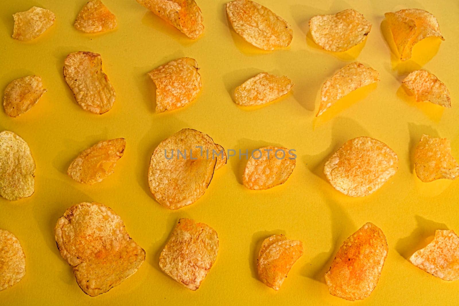 Close-up of potato chips or crisps on pastel yellow background.  Cinema concept with many potato chips on yellow retro background.