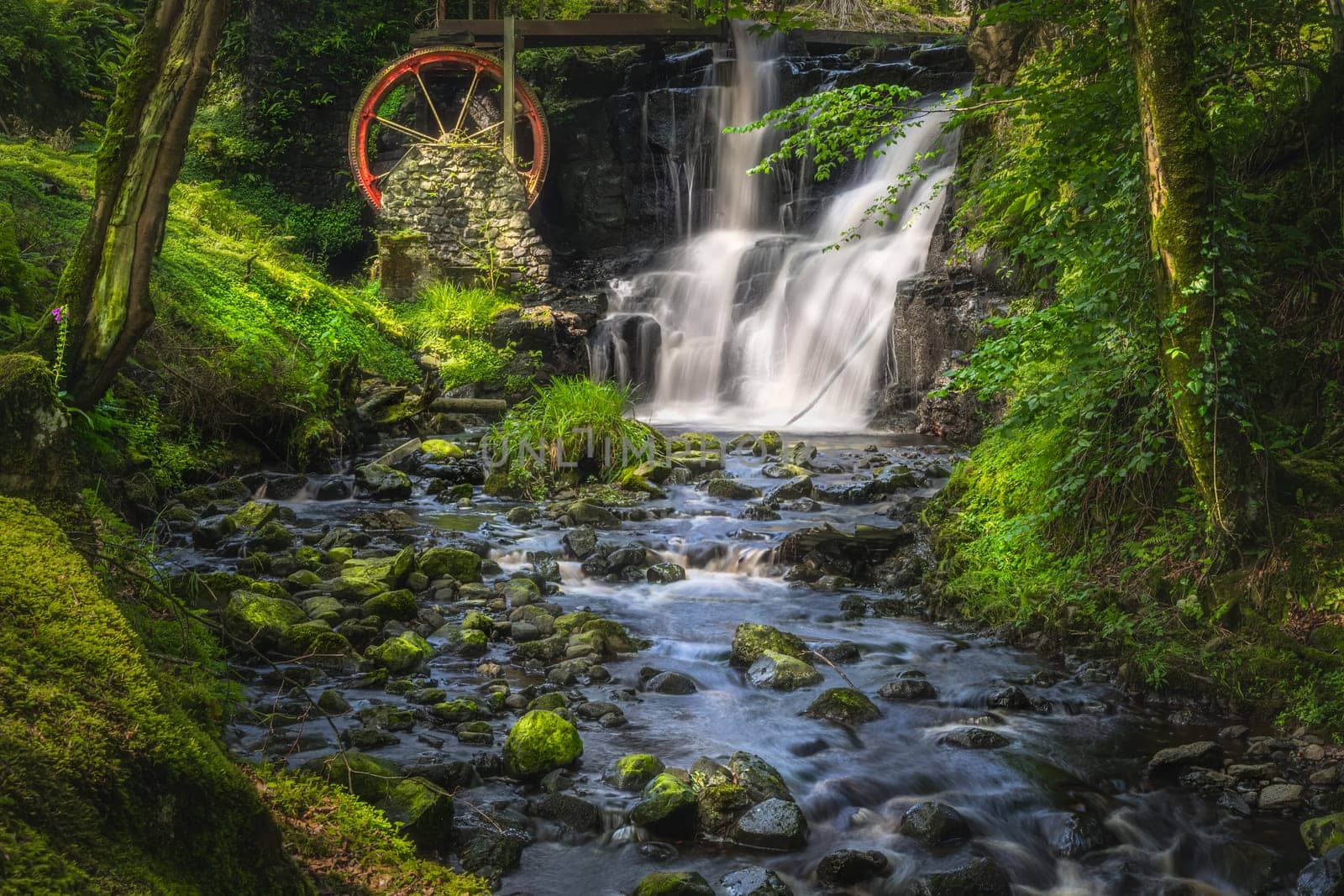Stream leading to red waterwheel and waterfall in Glenariff Forest Park, County Antrim, Northern Ireland. Long exposure and soft focus photography