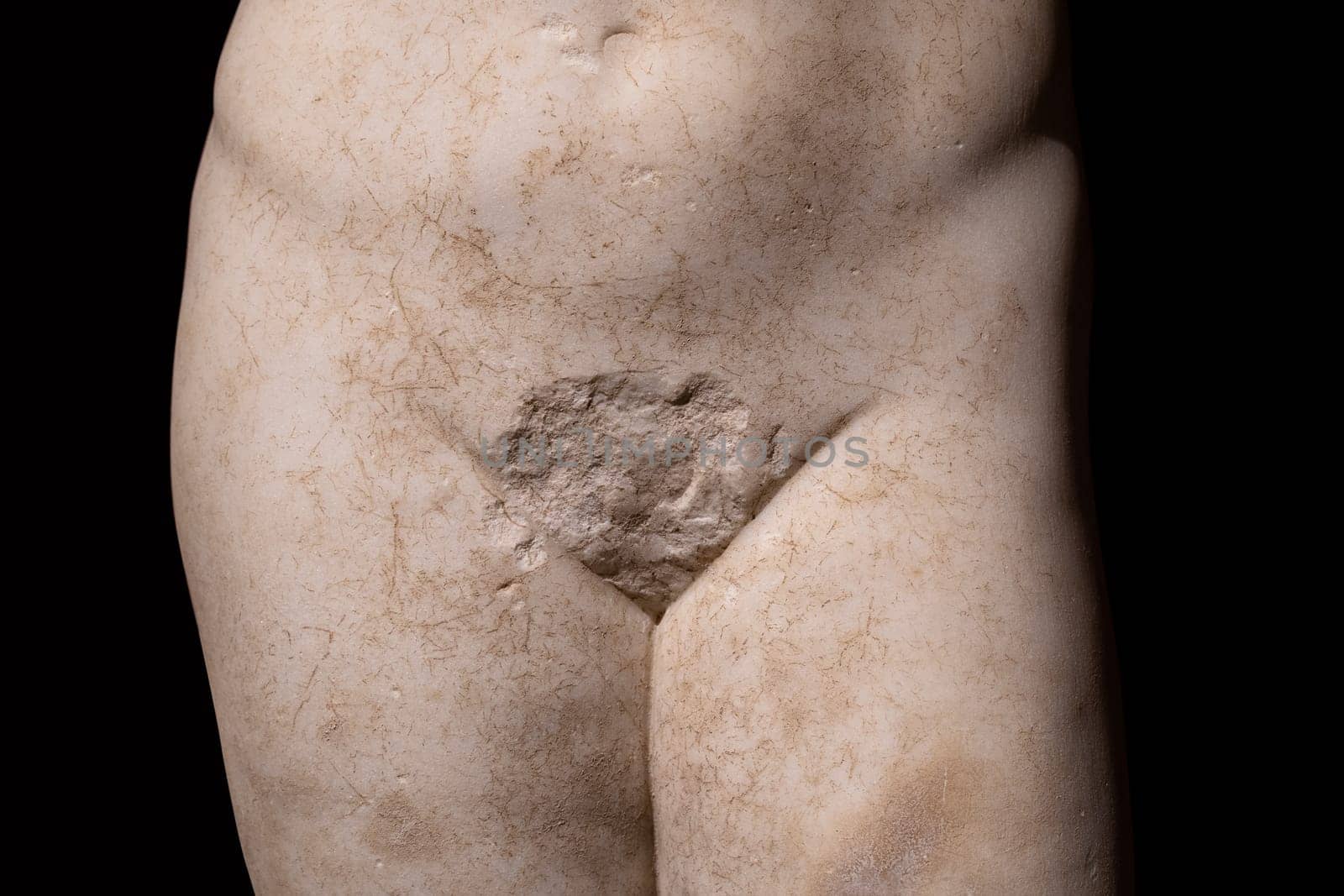 front view closeup detail of antique white marble human statue with genitalia missing on dark background metaphor for sexuality and gender