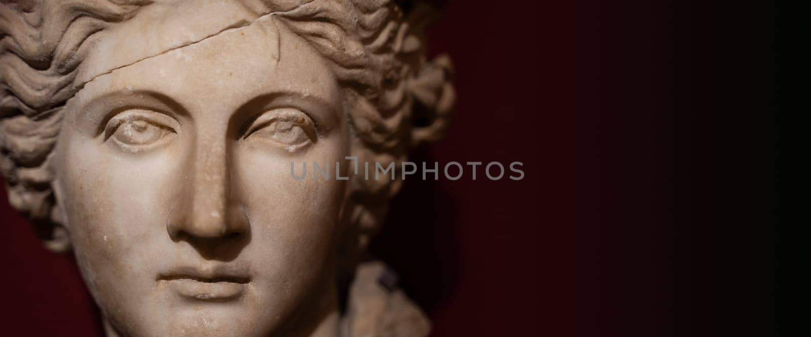 front view closeup of woman antique white marble statue with cracked forehead face and damaged eyes on dark background copy space available