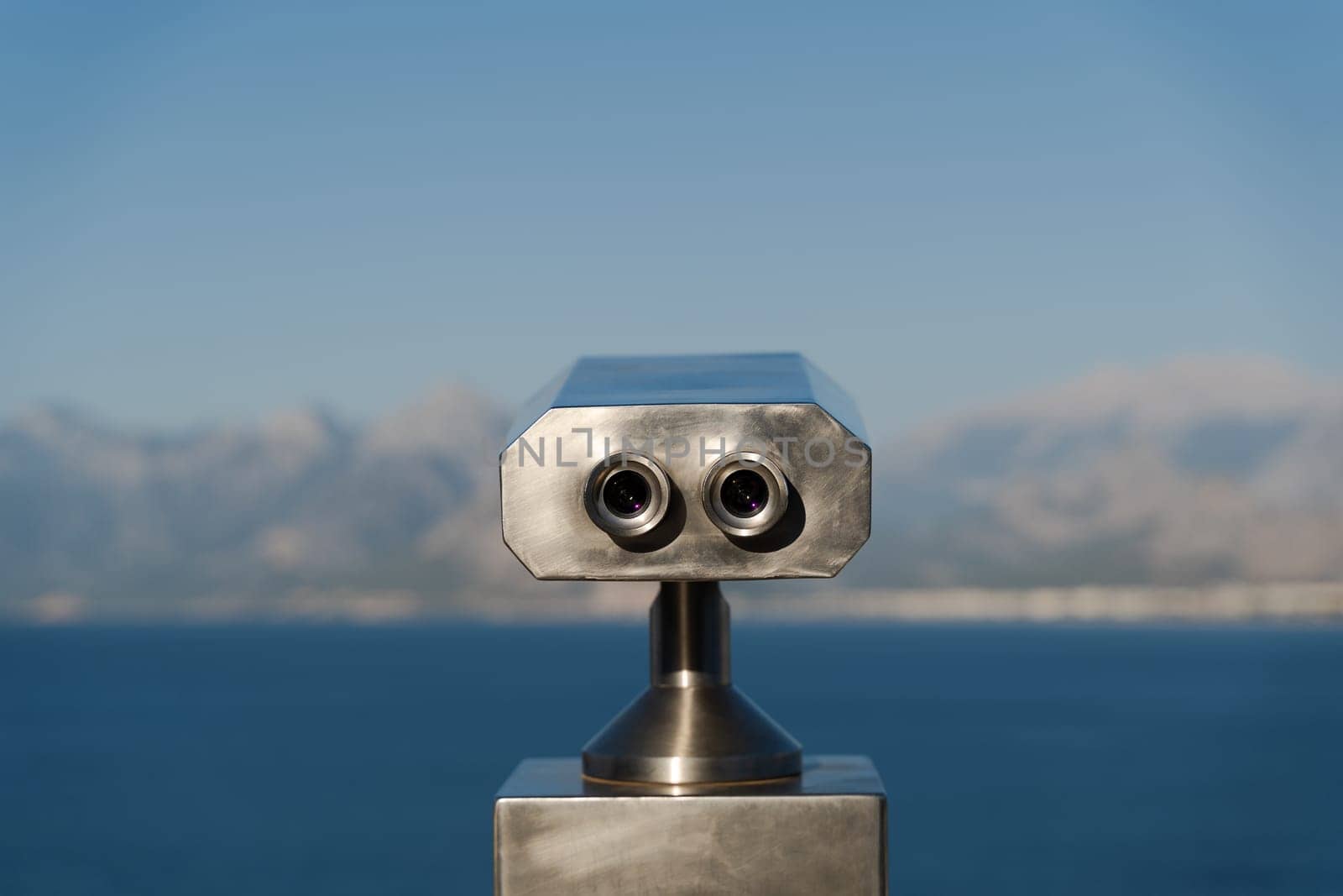rear view closeup of aluminum coin operated binoculars with beautiful sea and mountains landscape panorama in the background