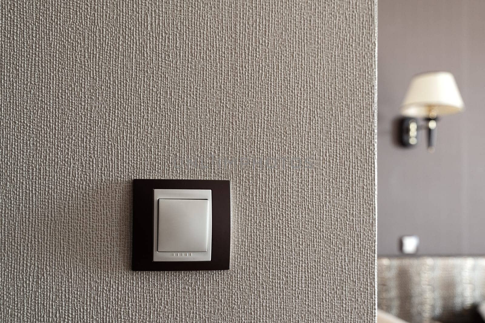 front view closeup of white light plastic switch socket on textured wall with home interior in the background