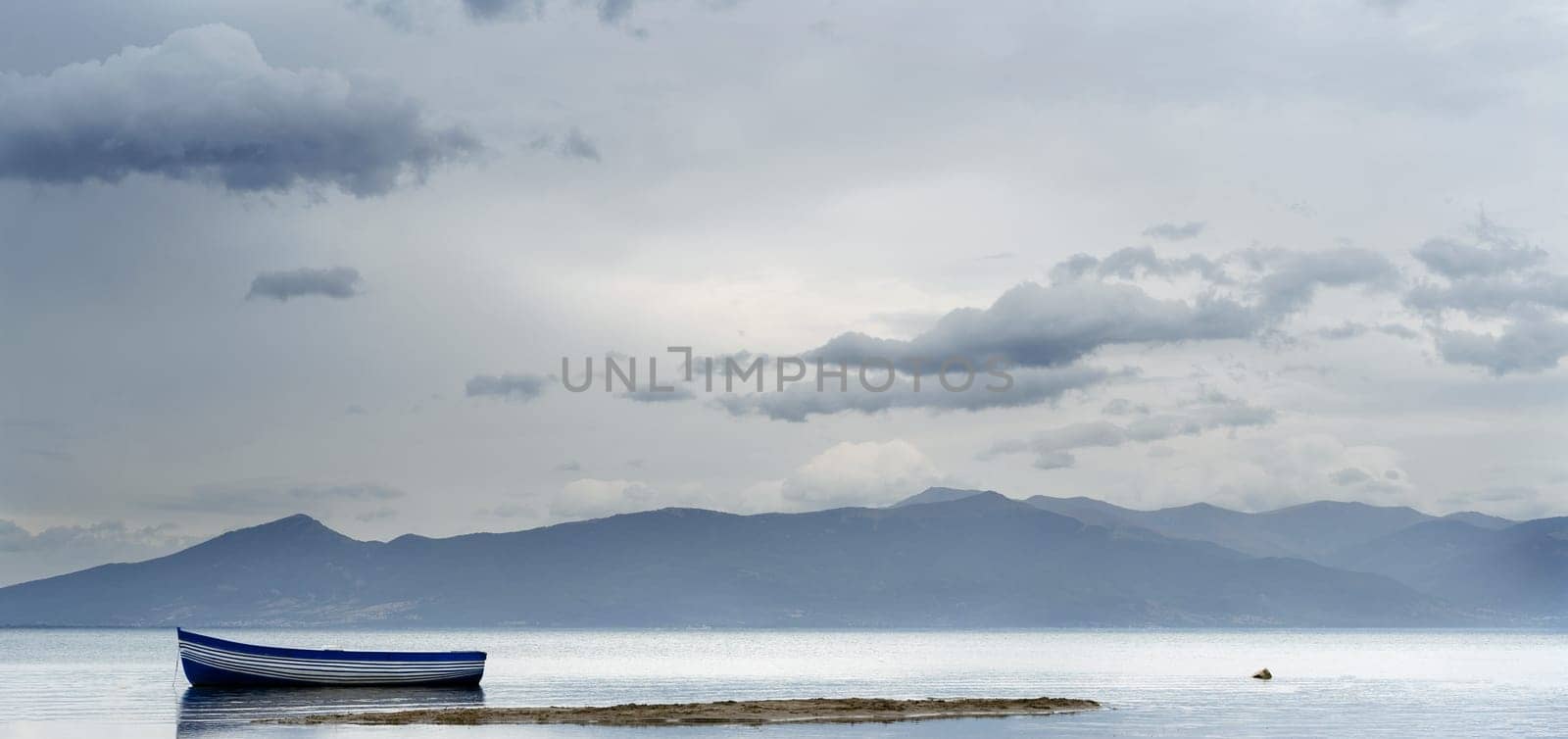 natural landscape with mountains and lonely boat with blue and white stripes on lake Prespa in North Macedonia