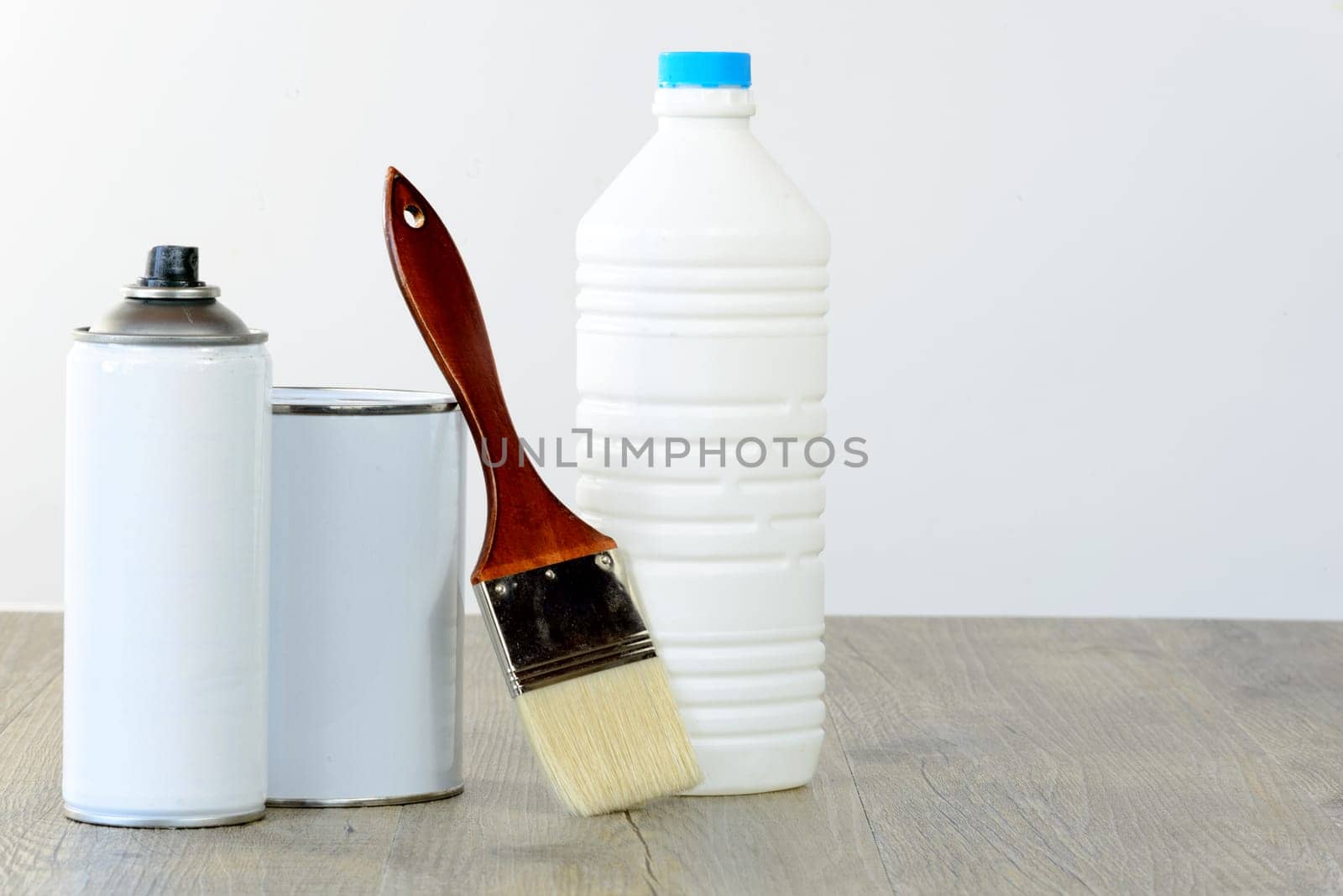 bottle, aerosol, paint pot and brush on wooden table
