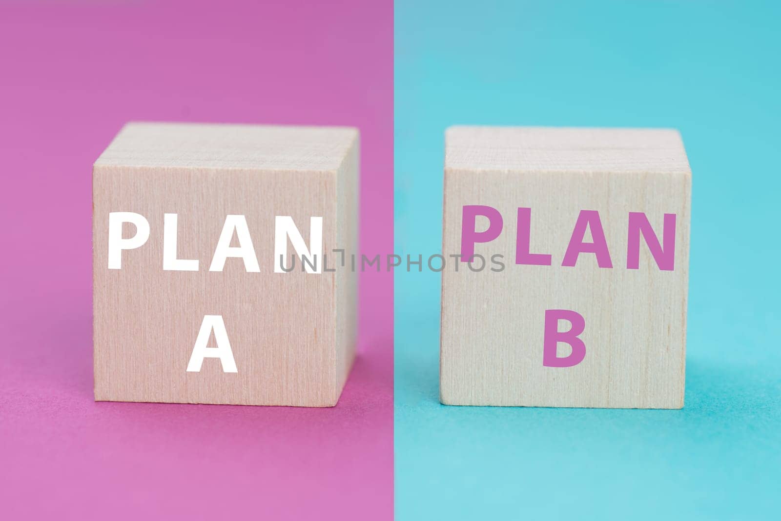 Plan A and B standing on wooden cubes, pink and blue colored background, options of possibilities