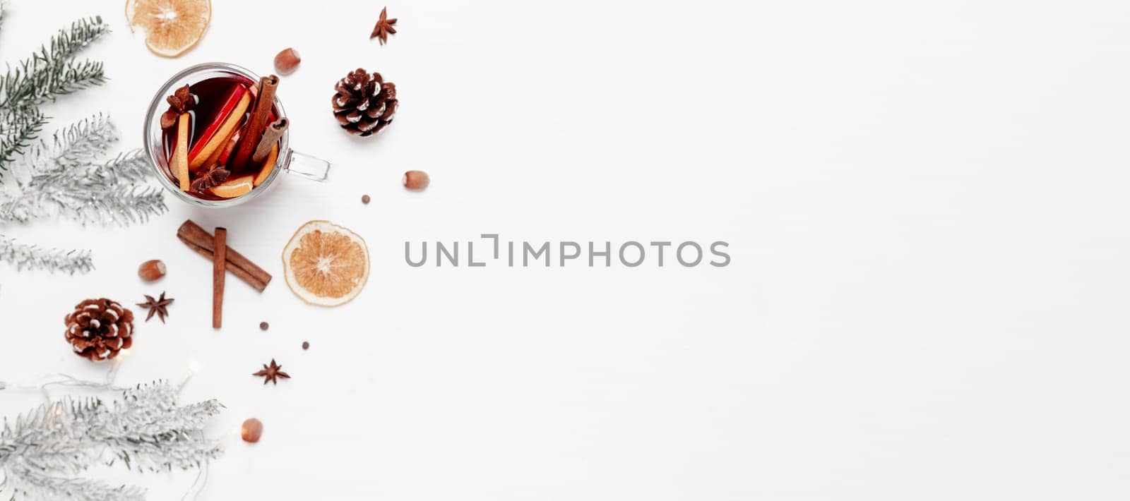 Christmas banner flat lay on white gray background with glass cup or mug of Mulled Wine, present red gift box, decorations, cinnamon, orange, apple, various spices, fir, cone, anise. Conceptual photo