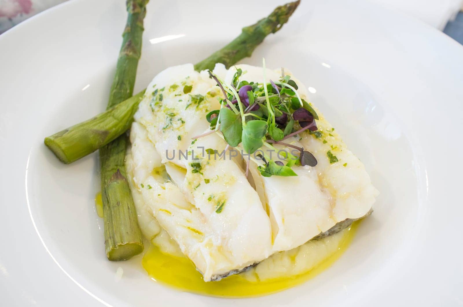 Oven-roasted codfish topped with green wild asparagus and corn salad. Closeup