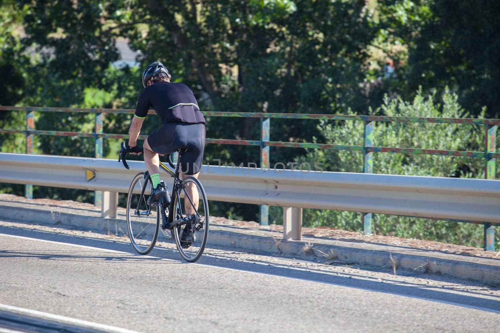 Mature biker crossing river bridge on local road. Road biking by Extremadura, Spain
