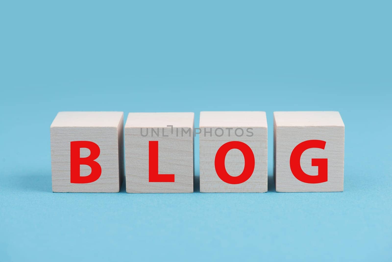 The word blog is standing in red colored letters on wooden cubes, blue background