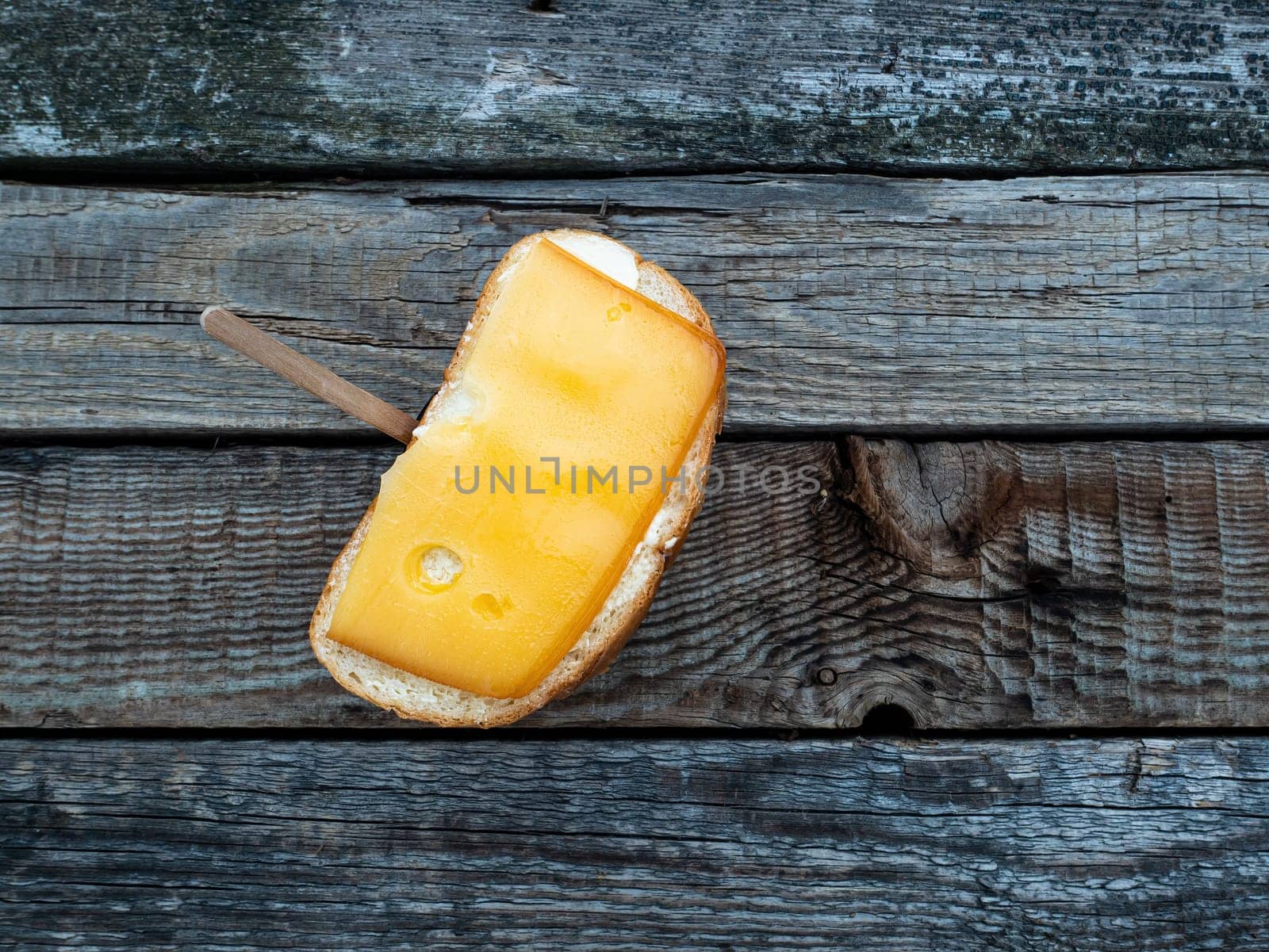 Hard cheese sandwich and a cup of coffee on a wooden table. Hard cheese. Butter. White bread. Cardboard coffee cup. Wooden table. Morning breakfast. Food intake. Street Cafe.