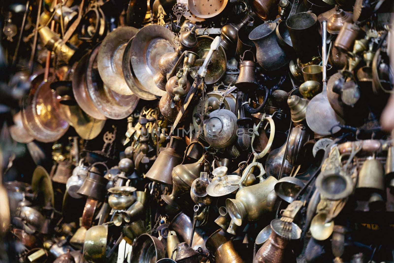 perspective view closeup of many different metallic antique pots plates and bowls of different sizes and shapes hanging on a wall in a shop