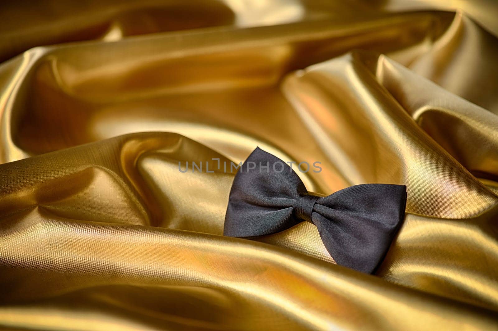 Black bow tie on draped golden satin