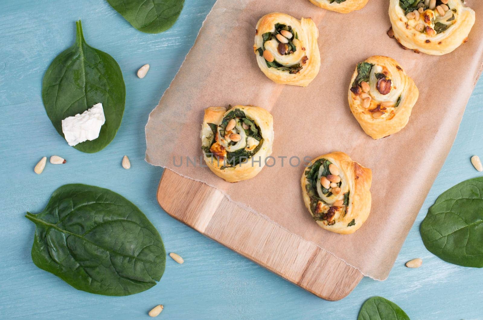 Puff pastry with spinach and feta cheese, rolled up to spirals, fresh from the oven, blue background