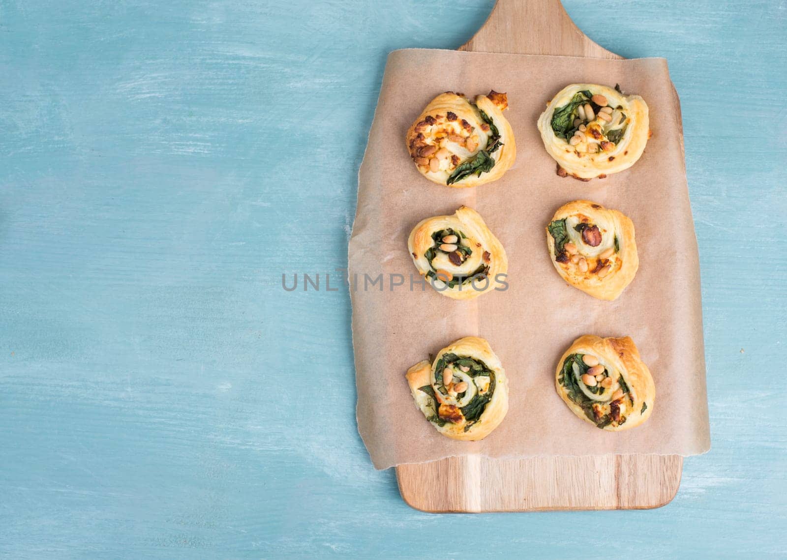 Puff pastry with spinach and feta cheese, rolled up to spirals, fresh from the oven, blue background