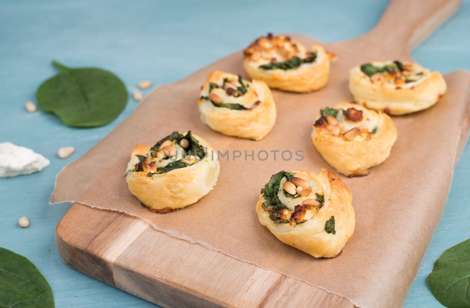 Puff pastry with spinach and feta cheese, rolled up to spirals, fresh from the oven, blue background