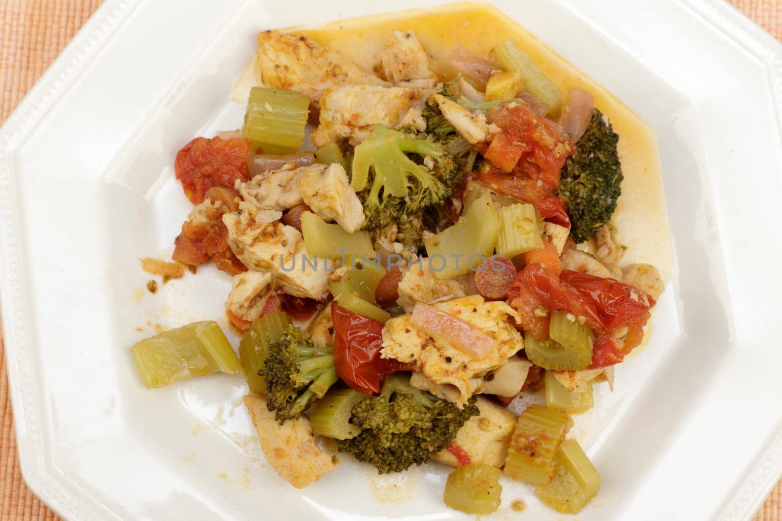 Close-up of ready-to-eat lunch of chicken meat with broccoli, carrots, onions, tomatoes and seasonings on an octagon plate. Cooked inner of lemon ginger chicken and mixed vegetable supper on a plate