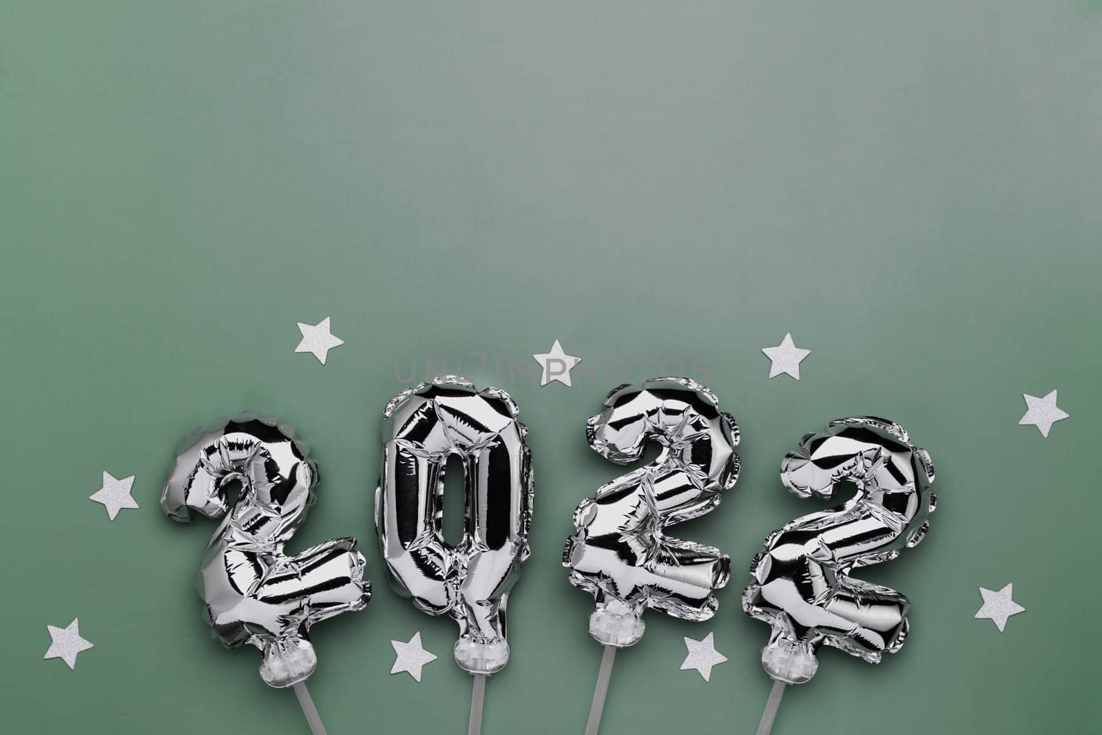 New Year 2022 or Christmas green background flat lay. Top view on 2022 balloon silver or metallic numbers on sticks with stars. Invitation or greeting card concept. Festive mood. High quality photo