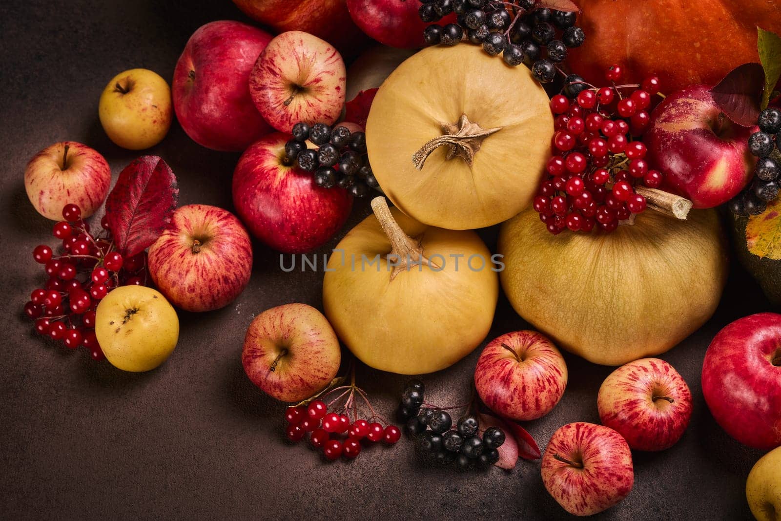 Thanksgiving background. Festive still life with pumpkins, berries, autumn leaves and apples on dark brown background. Happy Thanksgiving  day, autumn harvest, Halloween. Top view