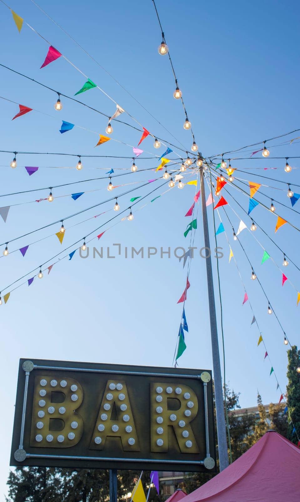 Bar banner with colorful pennants and light bulbs on pole. Outdoors party background