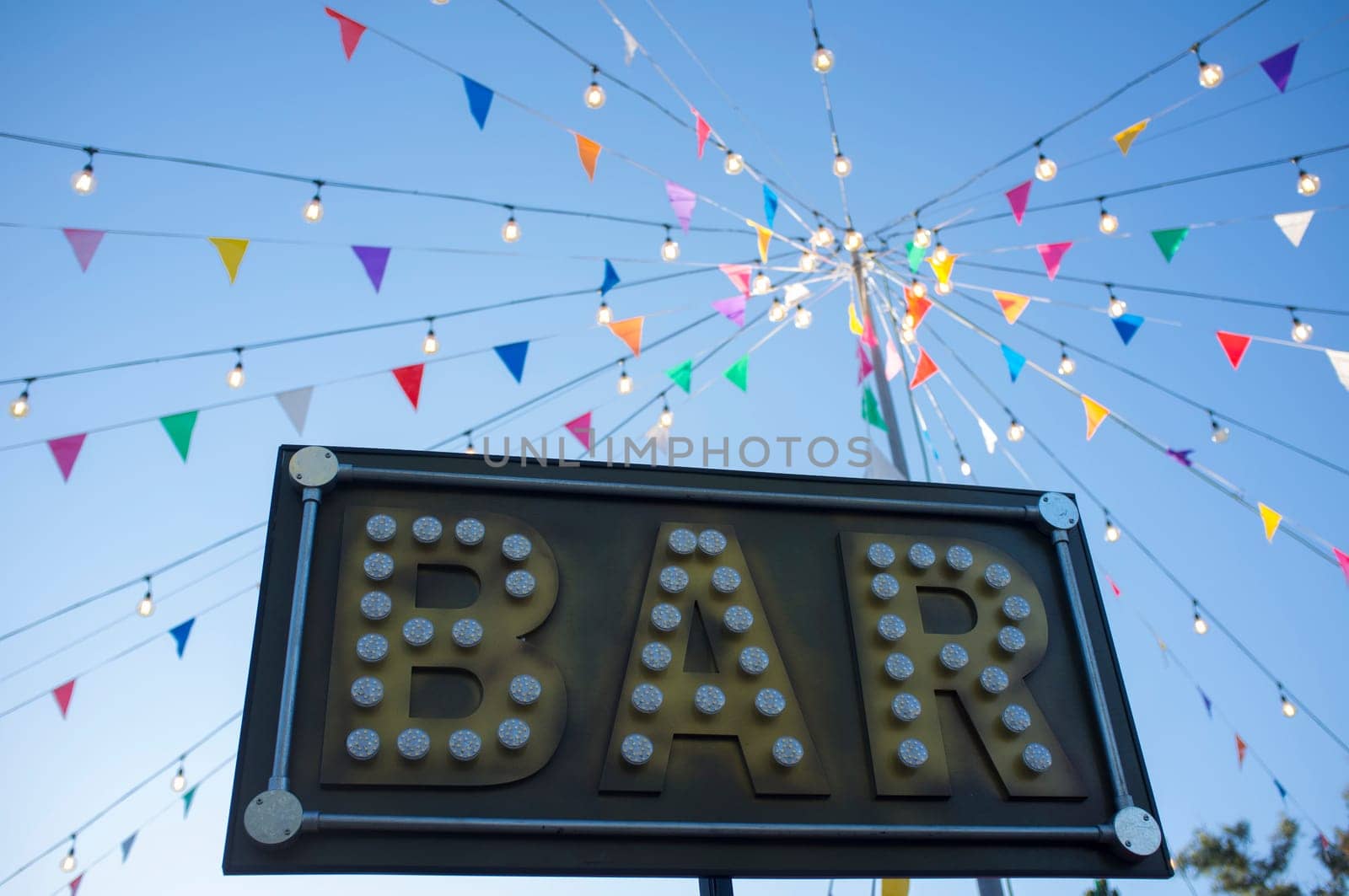 Bar banner with colorful pennants and light bulbs on pole. Outdoors party background
