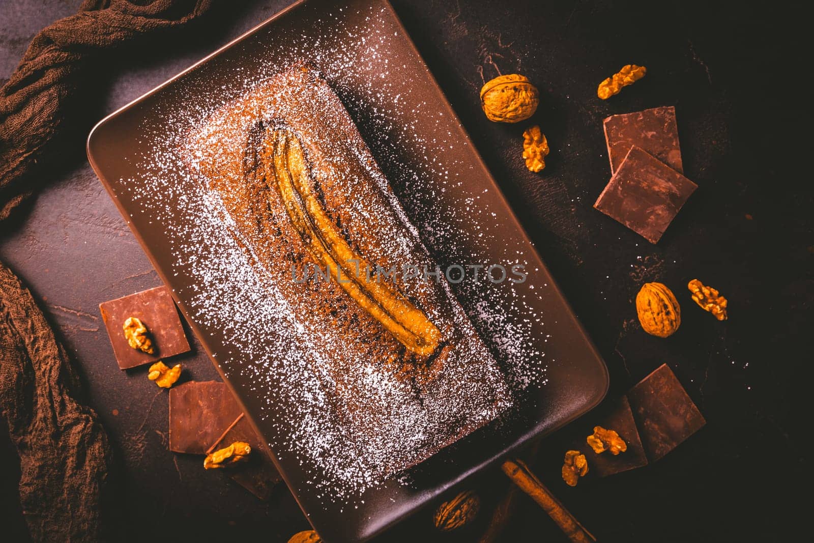 Homemade vegan banana bread or cake with nuts, chocolate and cinnamon on brown background