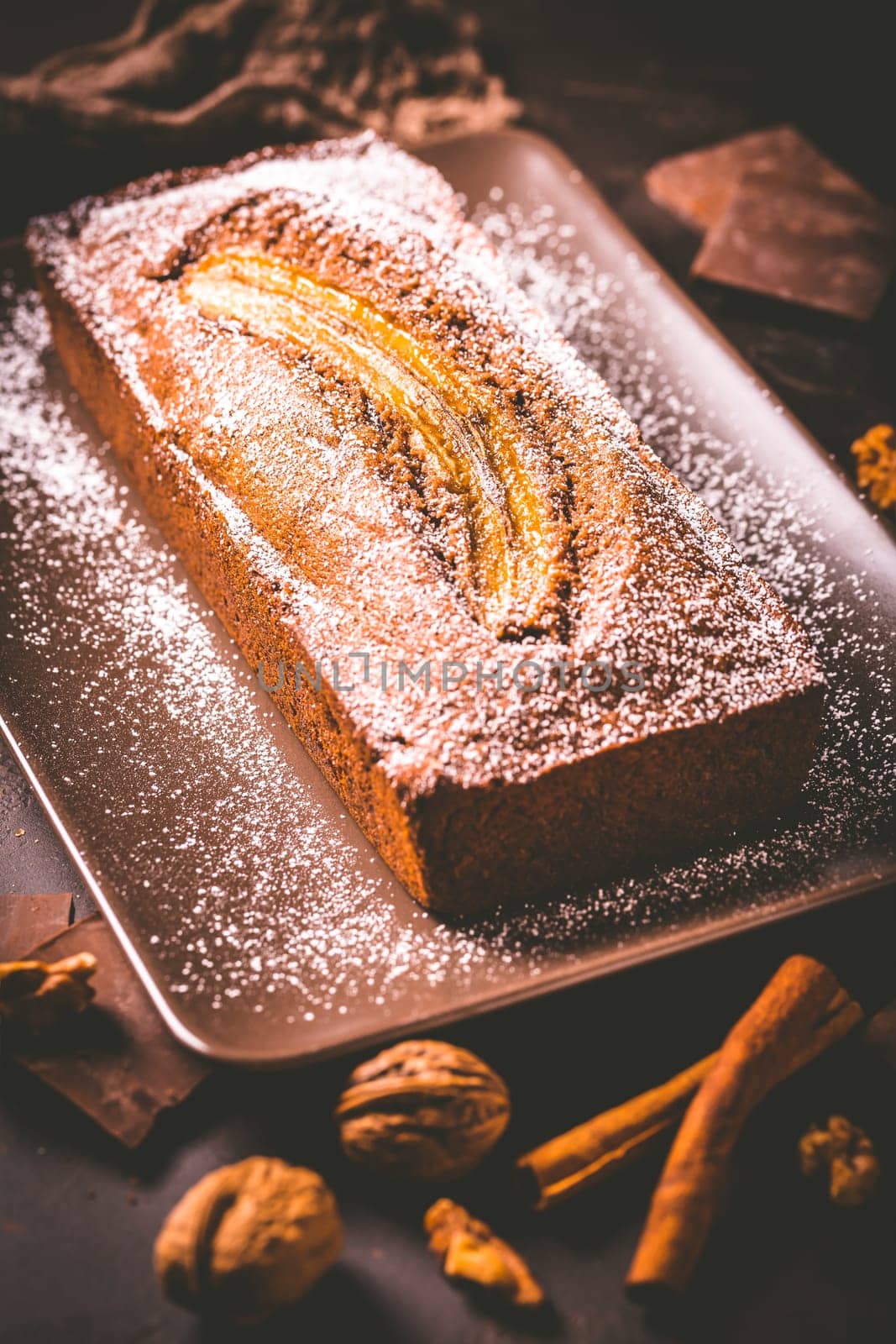 Homemade vegan banana bread or cake with nuts, chocolate and cinnamon on brown background