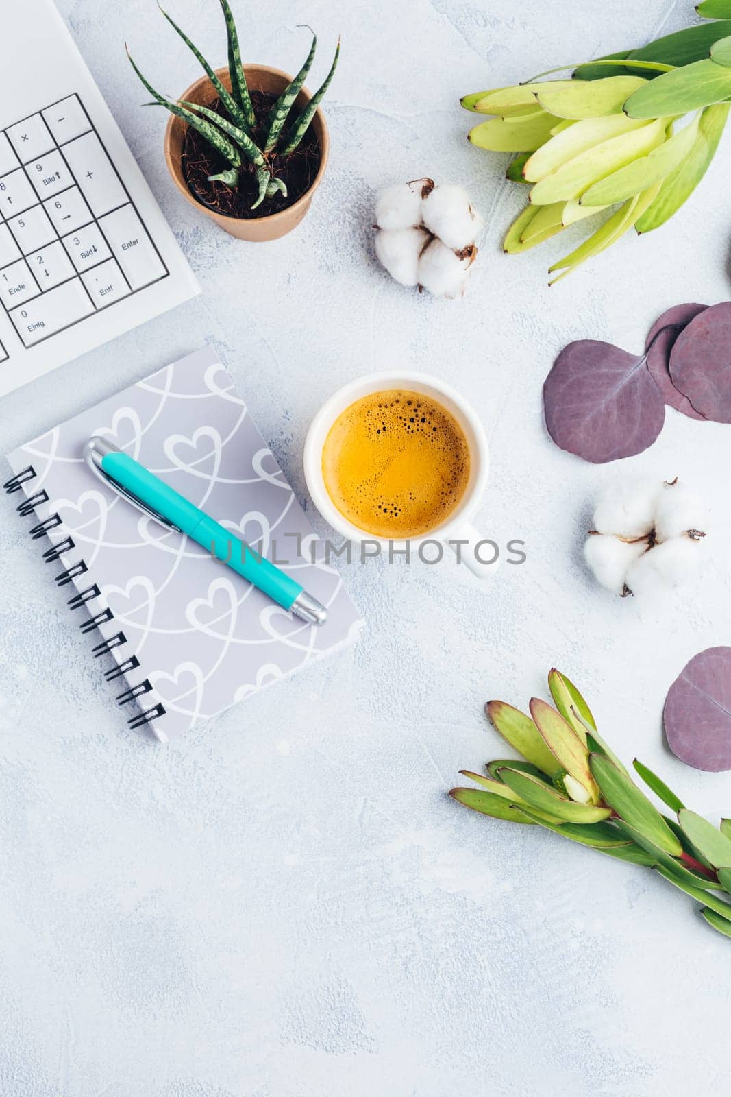 Workplace with cup of coffee, empty notebook, keyboard, supplies and flowers in bright tone
