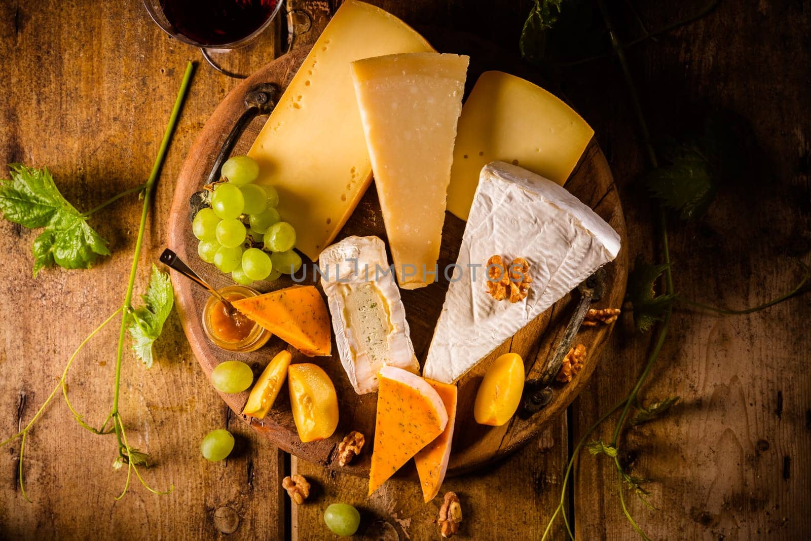 Cheese platter, assortment of different cheeses with glass of red wine, grapes on wooden table