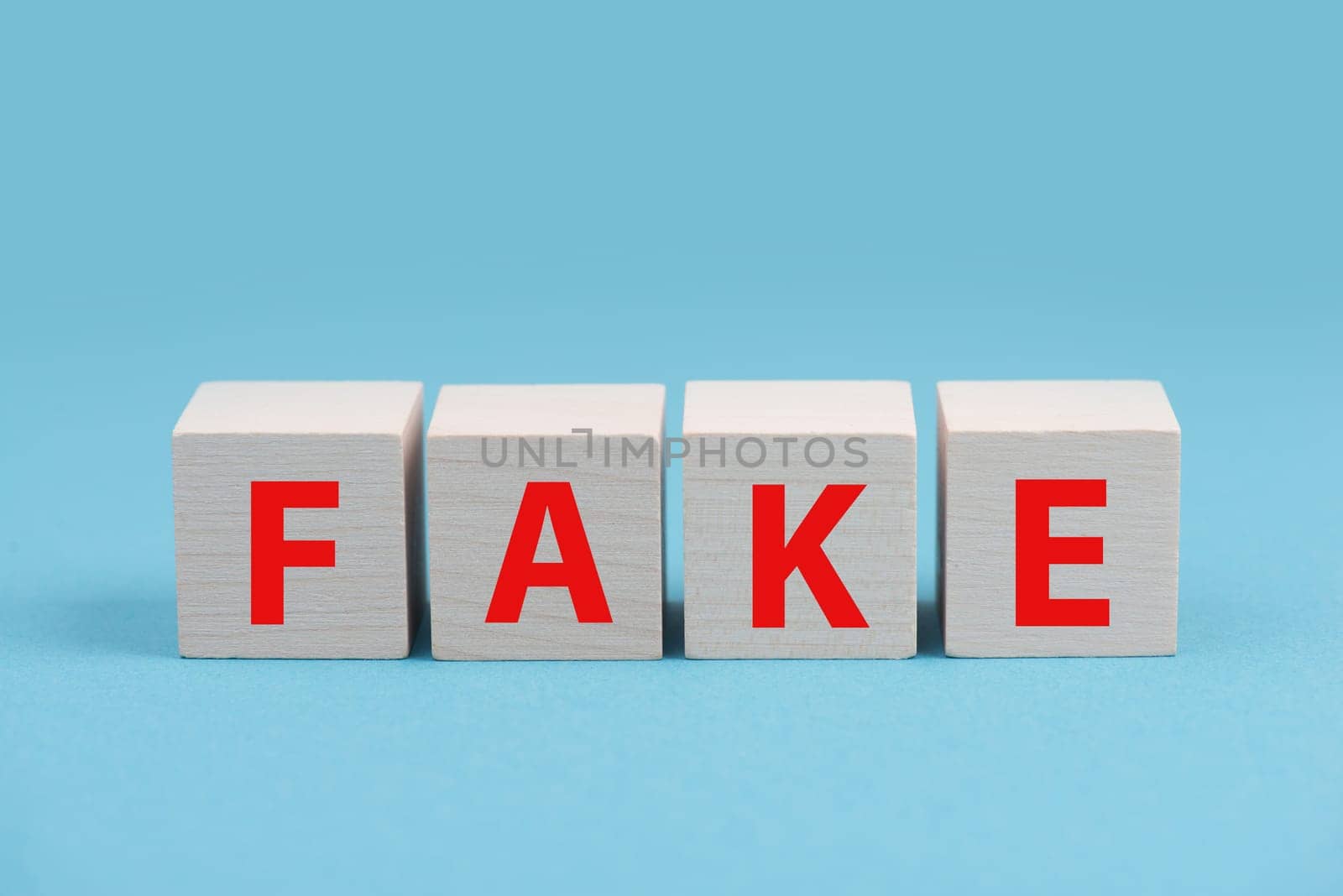 The word fake is standing in red color on wooden cubes, blue background