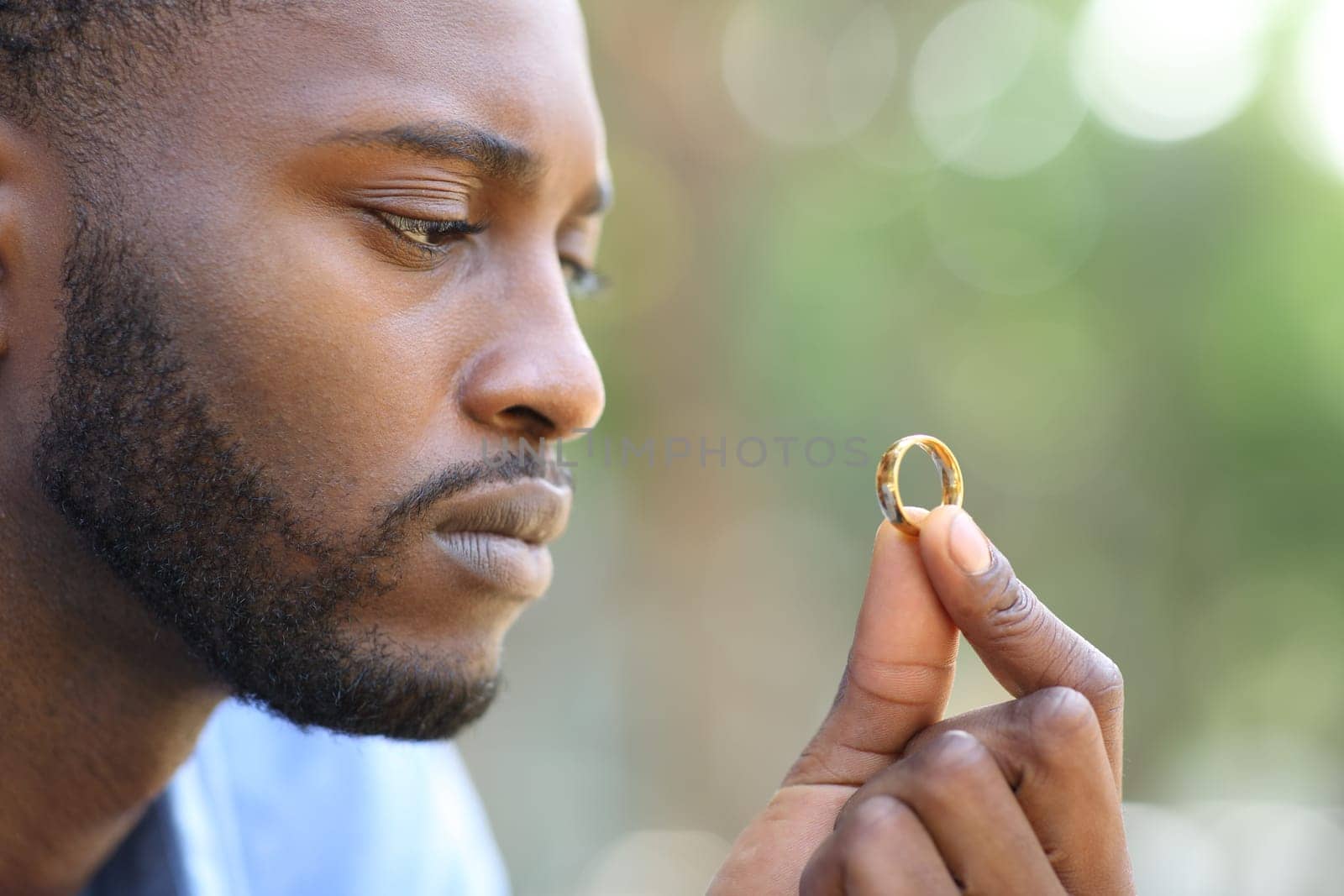 Sad black husband doubting holding wedding ring in a park