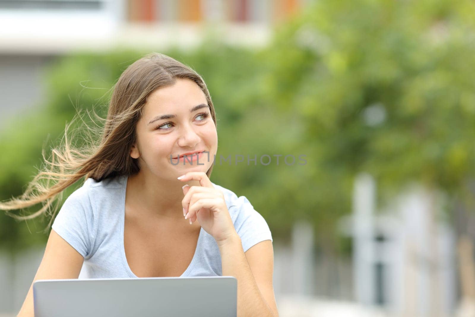 Happy teen with a laptop thinking looking at side in a park with copy space