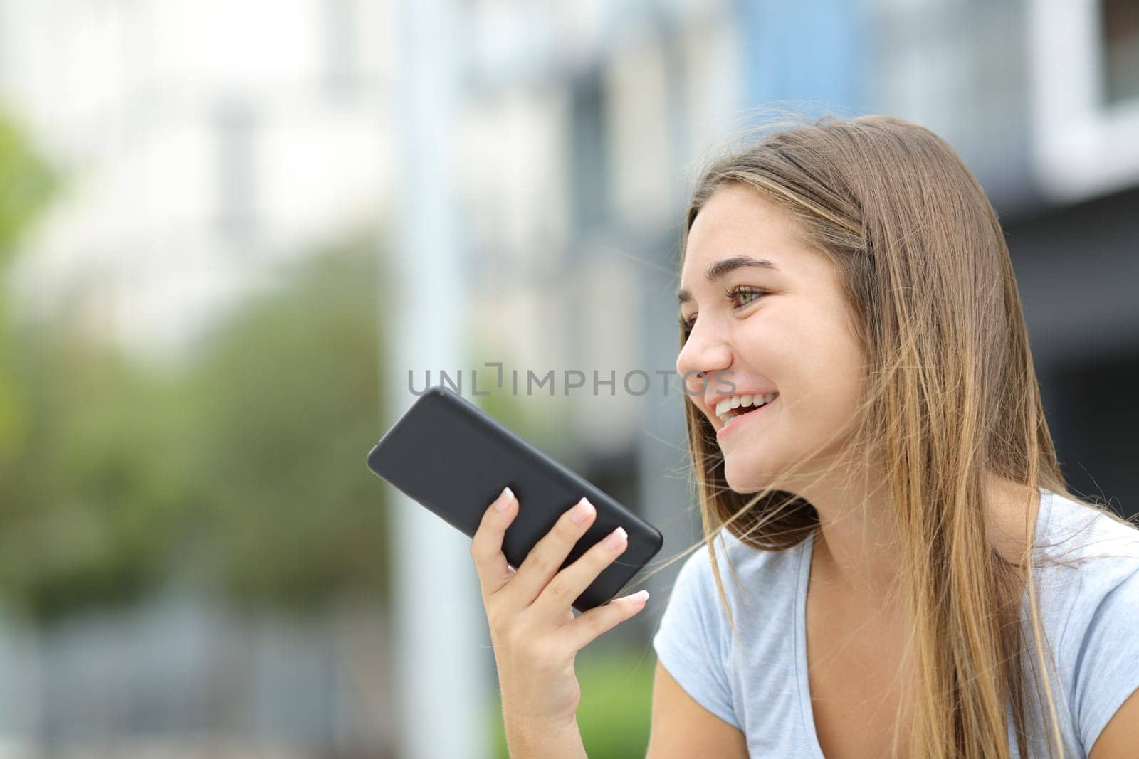 Happy teen using voice recognition on smart phone in the street