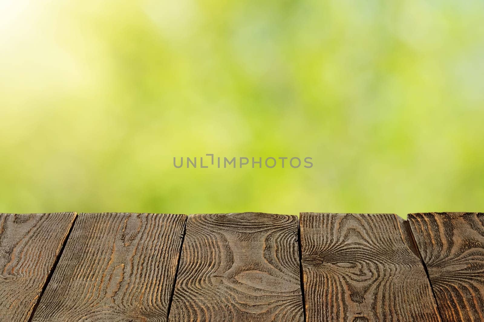 Background with blurred green leaves and empty wooden planks in the foreground. For product demonstrations, free space, layout, mockup, perspective board, background board.