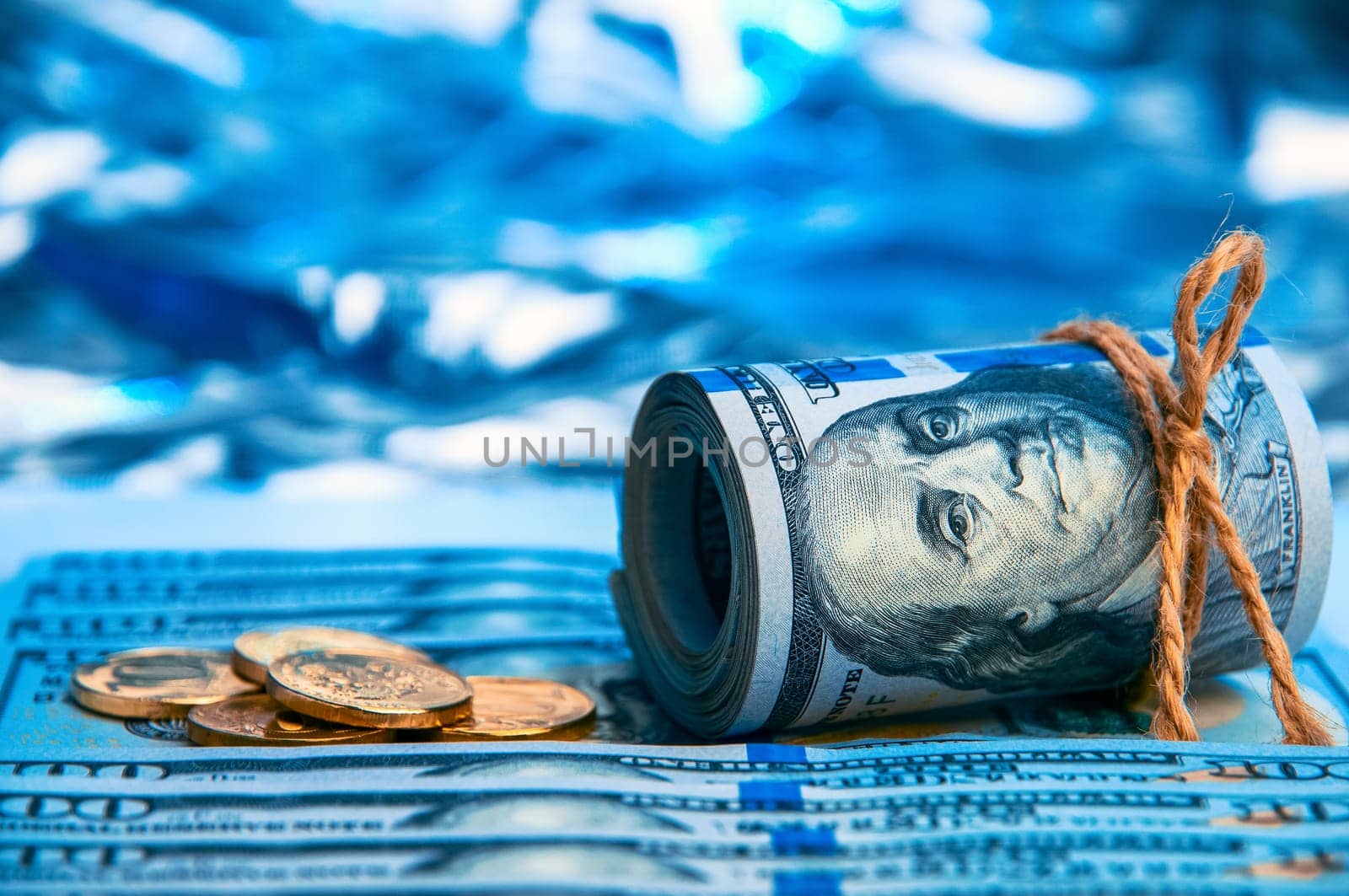 Dollars. A roll of hundred-dollar bills and scattered gold coins lying on the bills on a blue background with a side. Blue style.