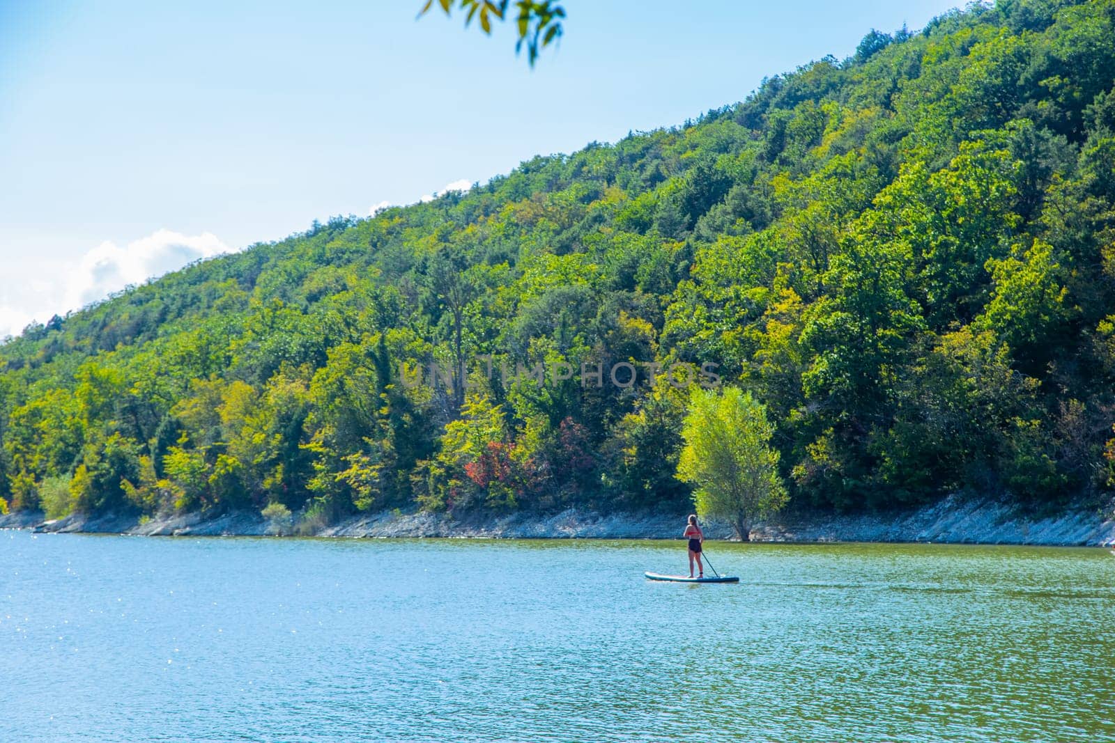 A girl is floating on a board on the river, in the background there are mountains overgrown with trees. High quality photo