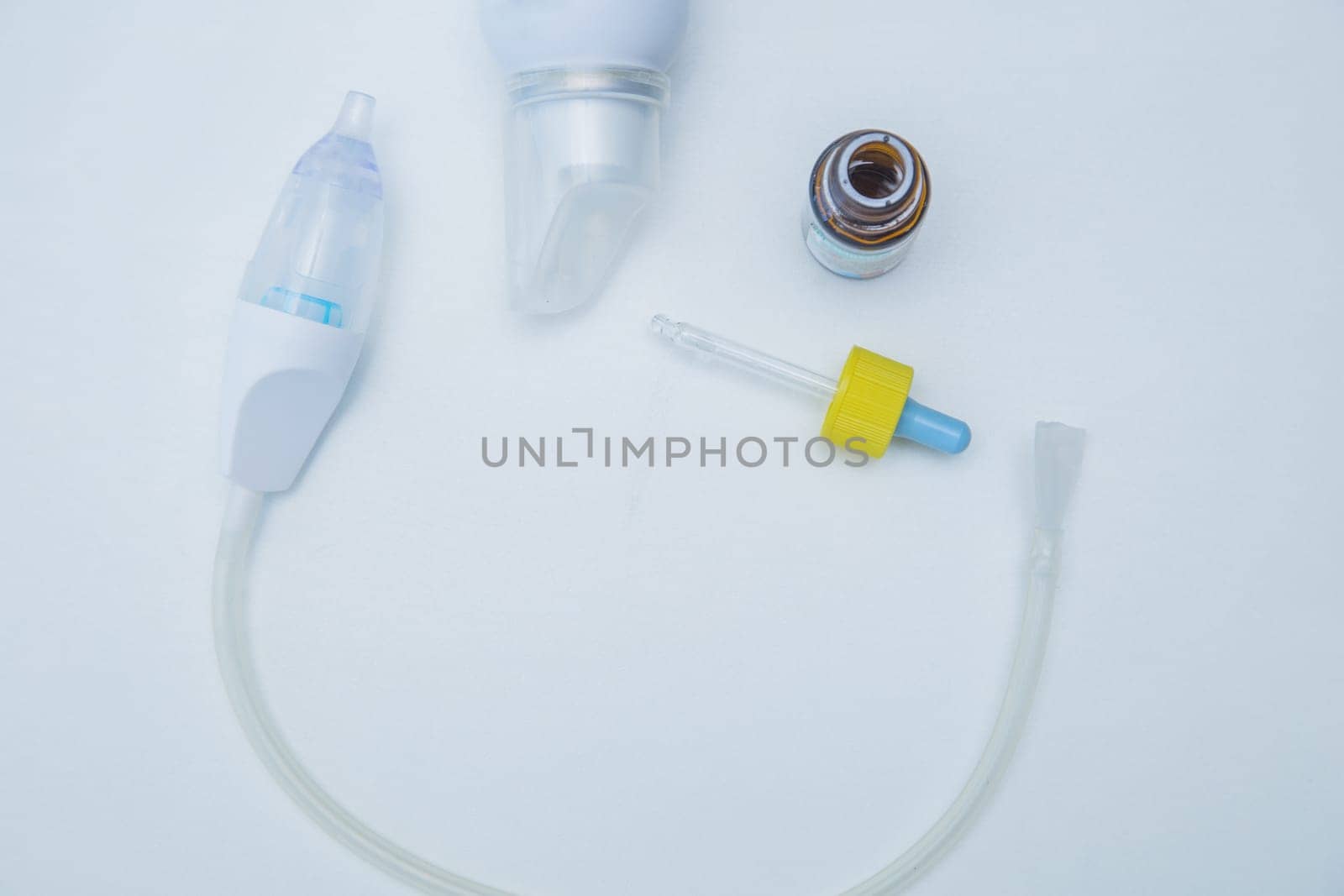 The children's aspirator lies in a semicircle on a white background, to the side of it are drops from a runny nose with a pipette and water for washing. High quality photo